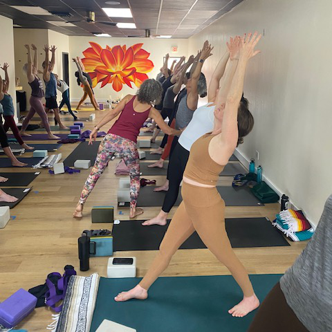 Phoenix Workshop 2026sq Students in a yoga workshop doing poses and receiving assists from the instructor